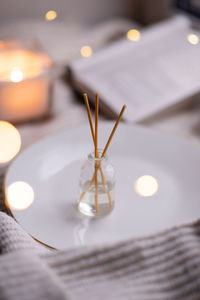 Home liquid perfume in glass bottle and wooden sticks with burning candle and open paper book 