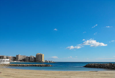 Scenic view of sea by buildings against blue sky