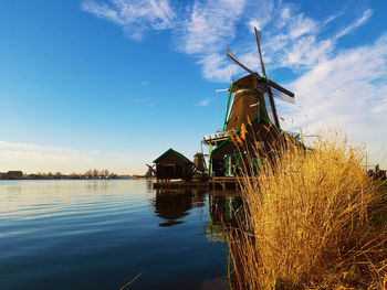 Traditional windmill by lake against sky