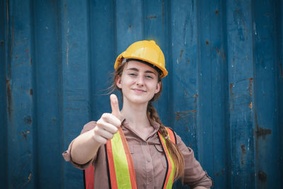 Portrait of a smiling young woman standing against blue wall