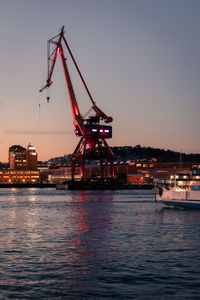 Cranes at commercial dock by river against sky during sunset