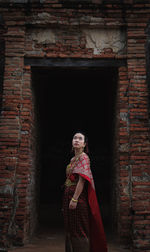 Side view of woman standing in traditional clothing against brick wall