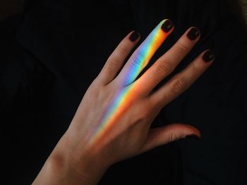 Colorful light on woman hand against black background