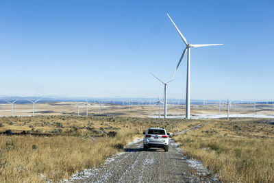 Wind turbines in field against blue sky with car