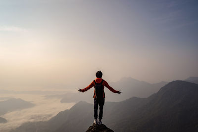 Rear view of carefree backpacker with arms outstretched looking at landscape while standing on mountain during foggy weather