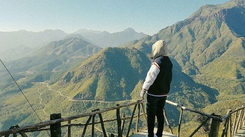 Rear view of man standing on railing against mountain