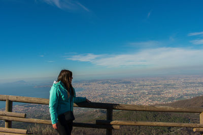 Mid adult woman standing by railing on observation point against blue sky during sunny day