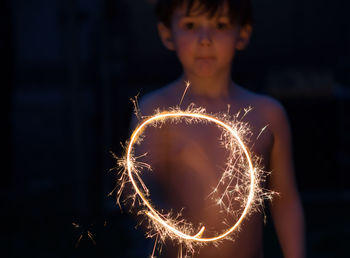 Portrait of shirtless boy spinning sparkler at night