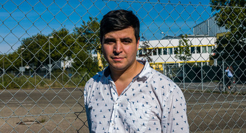 Portrait of man standing by chainlink fence