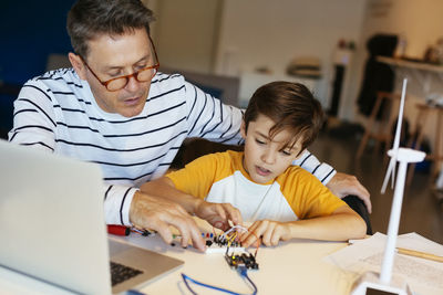 Father and son assembling a construction kit with laptop and wind turbine model