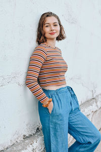 Portrait of smiling young woman standing against wall