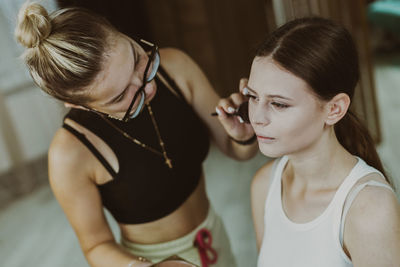 A young makeup artist applies powder with a brush to a girl s cheekbones.