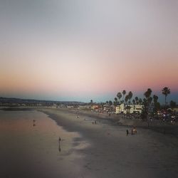People at beach against clear sky during sunset