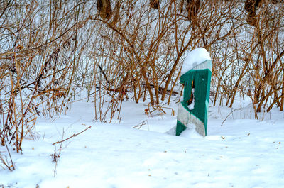 A wooden pillar is covered with snow cap near forest. winter landscape on meadow.