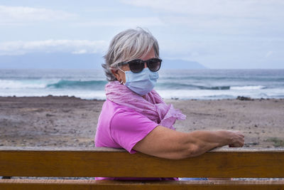 Portrait of senior woman wearing sunglasses siting on bench against sea and sky