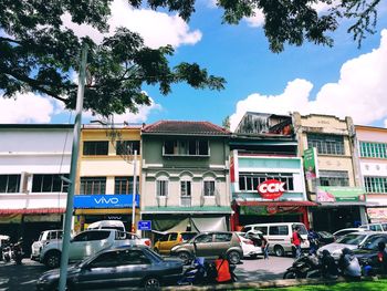 Cars on road by buildings in city against sky