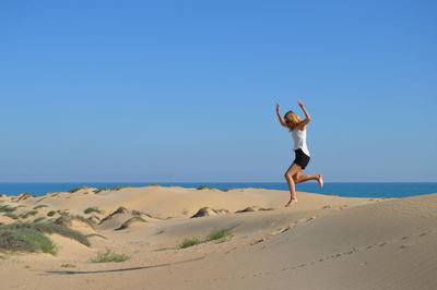 Full length of woman on sand at beach against clear blue sky