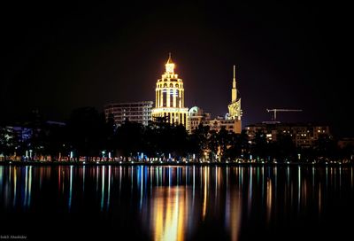 Illuminated buildings and lake against sky at night