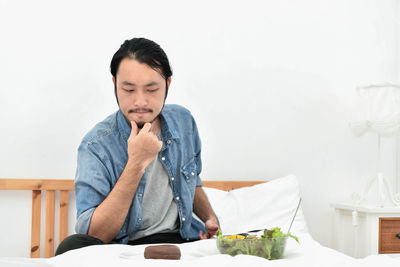 Thoughtful man looking at food while sitting against wall 