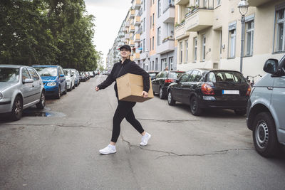 Confident delivery woman with cardboard box walking on street in city