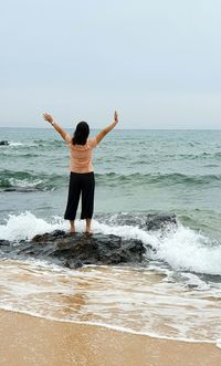 One person standing on a rock facing the sea surrounded by crashing waves.