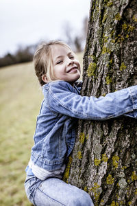 Portrait of smiling girl climbing tree on field