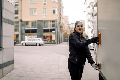 Portrait of confident young delivery woman with truck in city