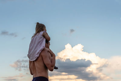 Rear view of man and little girl standing against sky