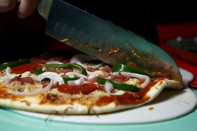 Cropped hand of person cutting pizza on table