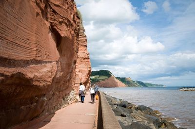 Rear view of women standing walking by sea against cloudy sky