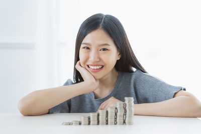 Portrait of smiling young woman by stacked coins at home