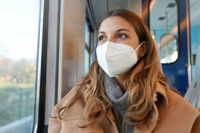 Lady wearing protective medical mask kn95 ffp2 on public transport looking through the window