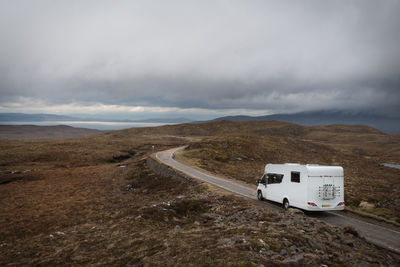 Car on road amidst landscape against cloudy sky