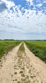 Dirt road amidst field against sky