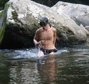 Shirtless man standing in river by rock