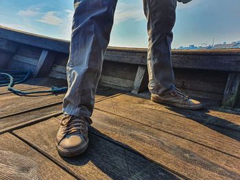 Low section of man standing on wood against sky