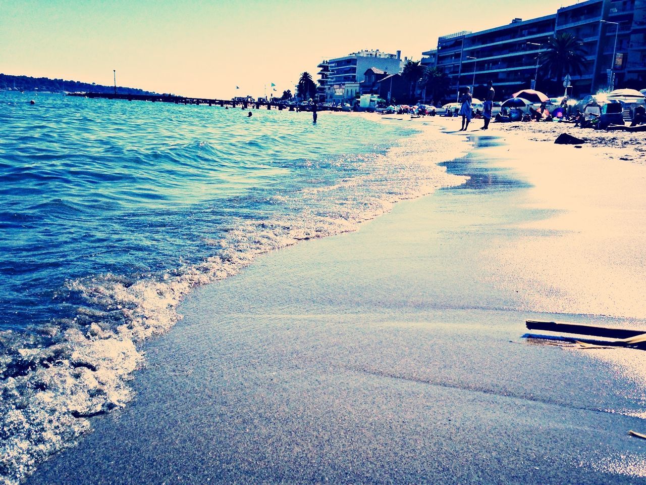 sea, beach, water, sand, shore, incidental people, horizon over water, building exterior, coastline, wave, sunlight, vacations, clear sky, sky, blue, tranquility, built structure, nature, scenics, person