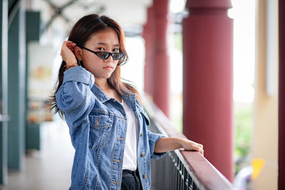 Portrait of beautiful young woman wearing sunglasses standing by railing