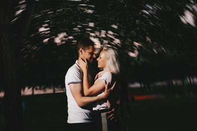 Couple embracing while standing against trees at dusk