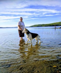 Woman standing with dog in lake against sky