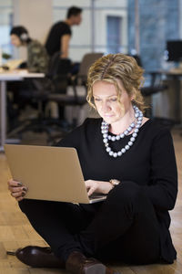 Full length of mature businesswoman using laptop while sitting on floor at office