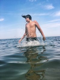 Full length of shirtless man in sea against sky