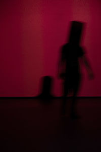 Blurred motion of silhouette man standing against red wall