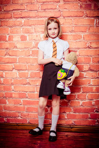 Full length portrait of schoolgirl standing against brick wall