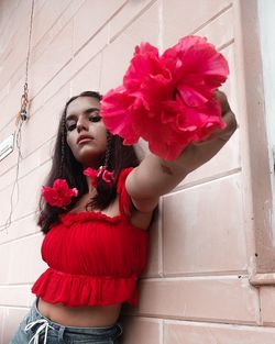 Young woman with pink flower standing against wall