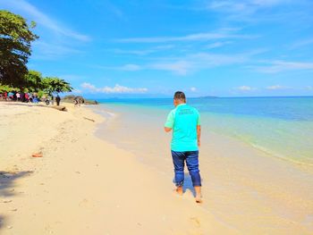 Rear view of man walking on shore at beach against sky