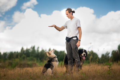Man playing with dogs while standing on grassy land against cloudy sky