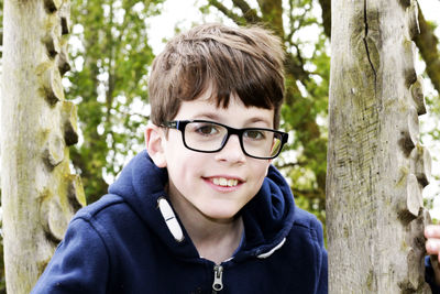 Portrait of boy wearing eyeglasses by tree trunk