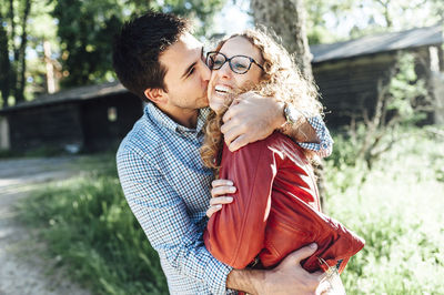 Man kissing cheerful girlfriend while standing in backyard