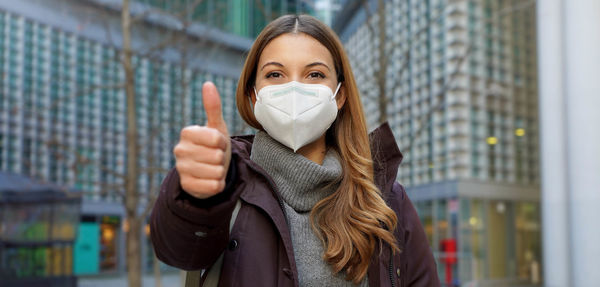 Banner cropped view of thumbs up woman wearing protective face mask and winter clothes in the city